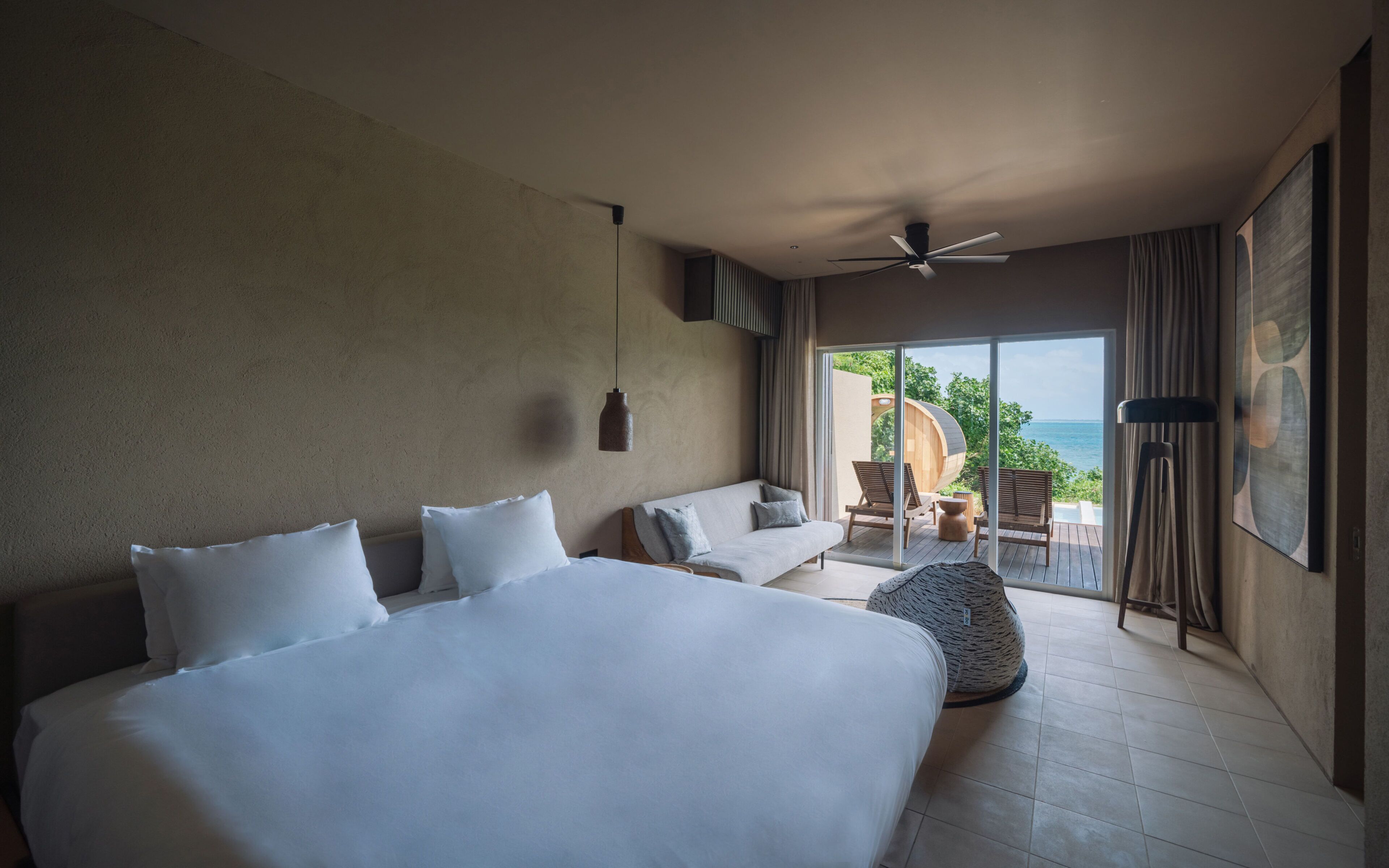 Een hotelkamer met een groot bed, een bank, een plafondventilator en uitzicht op de oceaan.