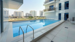 A modern residential building with a rooftop swimming pool, balconies, and a view of surrounding high-rise buildings. - Calm Balcony Apartment with Pool Access (Dubai)