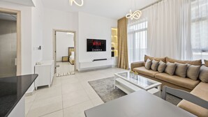 A modern living room with a sofa, coffee table, and a flat-screen TV mounted on the wall. - Calm Balcony Apartment with Pool Access (Dubai)