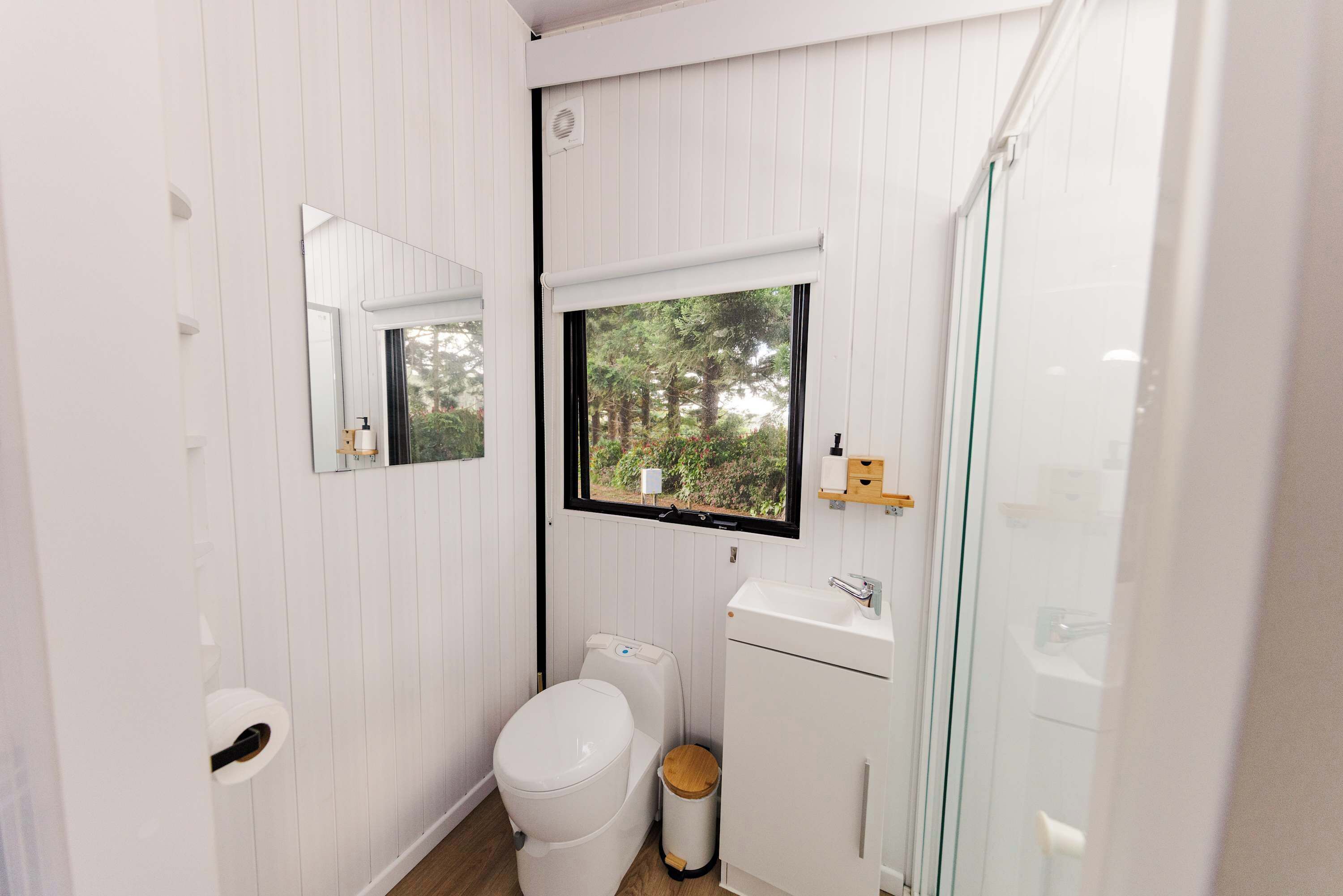 Ein kleines Badezimmer mit Toilette, Waschbecken und einem Fenster mit Blick auf Bäume.