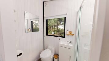 Ein kleines Badezimmer mit Toilette, Waschbecken und einem Fenster mit Blick auf Bäume.