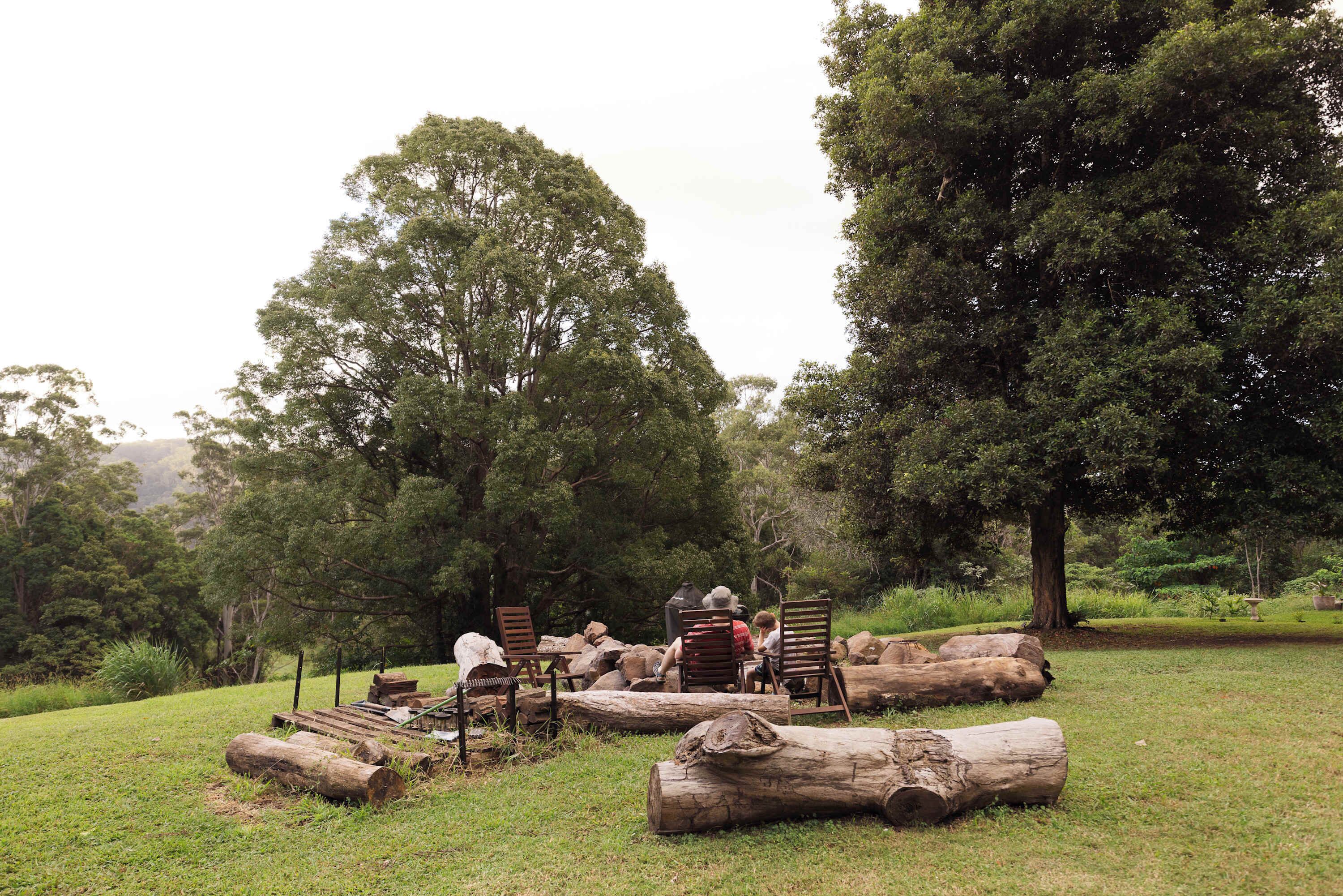 A group of people seated on wooden chairs in a grassy outdoor area with trees in the background.