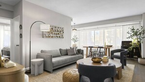 Un salon moderne avec un canapé gris, une table basse ronde et un coin repas comprenant une table et des chaises en bois.