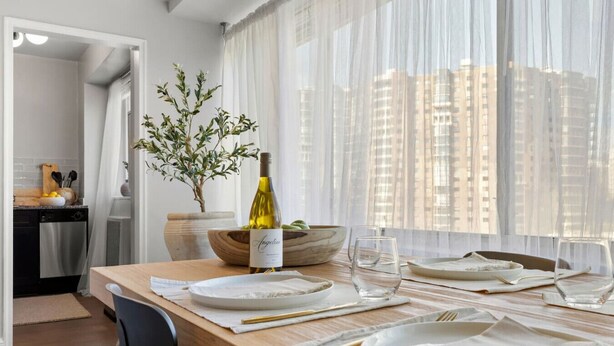 Un coin repas avec une table en bois dressée pour deux personnes, une bouteille de vin et un saladier rempli de fruits.