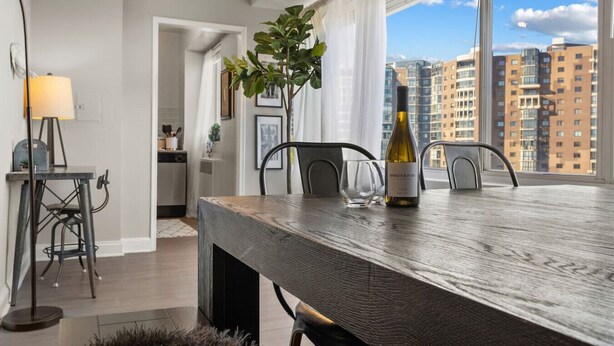 A modern dining area with a wooden table, chairs, a wine bottle, and a view of high-rise buildings. - Elevated Minimalist Escape, Free Parking & Metro (Arlington)