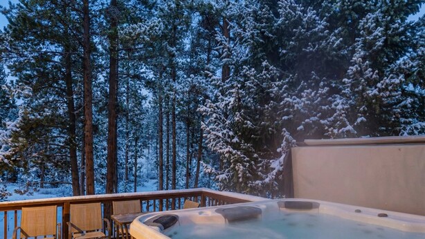 A hot tub on a wooden deck with chairs, surrounded by snow-covered trees. - Breckenridge Basecamp | Hot Tub + Fire Pit (Breckenridge)