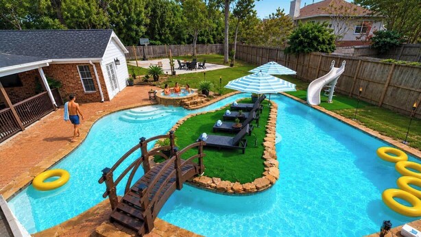 A backyard swimming pool with a slide, lounge chairs, and a wooden bridge. - Nasa Entertainment Escape: Games, Lazy River Pool (Seabrook)