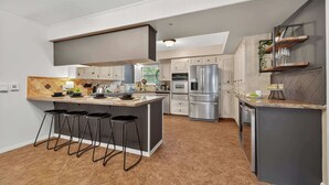 A modern kitchen with a central island, bar stools, stainless steel appliances, and a built-in oven. - Nasa Entertainment Escape: Games, Lazy River Pool (Seabrook)