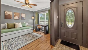 A room with a ceiling fan, a sofa with cushions, a desk with a chair, a window with curtains, and a door with a stained glass window. - Nasa Entertainment Escape: Games, Lazy River Pool (Seabrook)