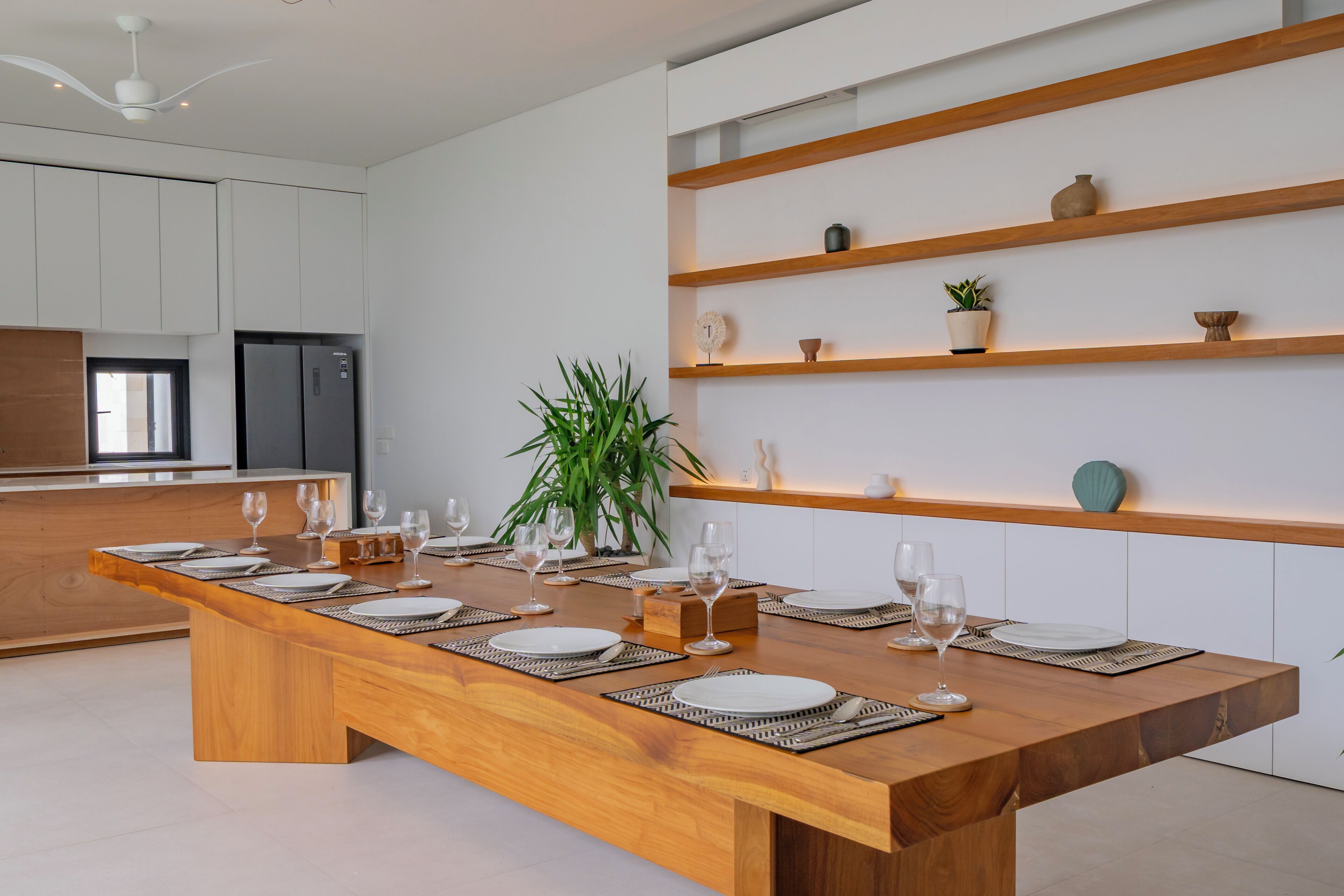 A modern kitchen with a wooden dining table set for six, white cabinets, and built-in shelves with decorative items.