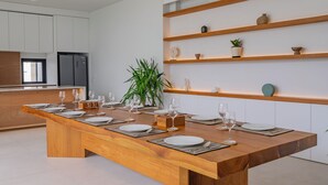 A modern kitchen with a wooden dining table set for six, white cabinets, and built-in shelves with decorative items. - Villa Shanaya Pererenan (Canggu)