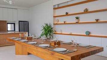 A modern kitchen with a wooden dining table set for six, white cabinets, and built-in shelves with decorative items.