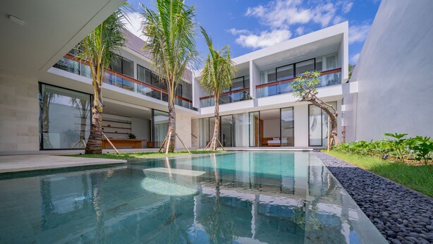A modern pool area with clear water, surrounded by palm trees and a multi-story building with large windows. - Villa Shanaya Pererenan (Canggu)