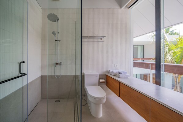 Un baño moderno con cabina de ducha de vidrio, inodoro y tocador de madera con espejo.