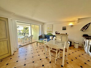 Un espacio habitable compacto con comedor, sofá, lavadora y balcón con mobiliario exterior.