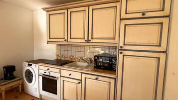 A compact kitchen with beige cabinets, a washing machine, a microwave, and a coffee maker.