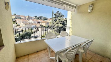 Un balcón con una mesa y sillas blancas, vista a una zona residencial y una farola.