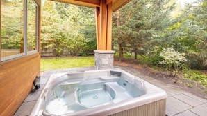 A hot tub under a wooden pergola with a stone pillar, surrounded by a garden with trees and shrubs. - NEW, Luxury Chalet, 5 mins to Village! (Whistler)