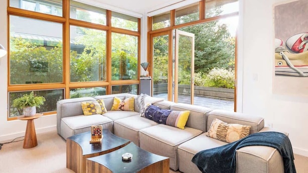 A modern living room with large windows, a sectional sofa, a coffee table, and a small side table with a plant. - NEW, Luxury Chalet, 5 mins to Village! (Whistler)