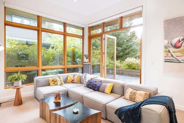 A modern living room with large windows, a sectional sofa, a coffee table, and a small side table with a plant.