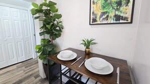 Un'area pranzo con un tavolo di legno apparecchiato per due persone, una pianta in vaso e un quadro astratto appeso alla parete.