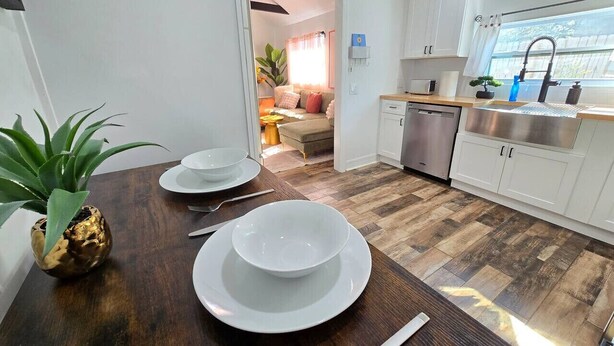 Una cucina moderna con mobili bianchi, un tavolo da pranzo in legno apparecchiato con piatti bianchi e un coltello, e una pianta in vaso.