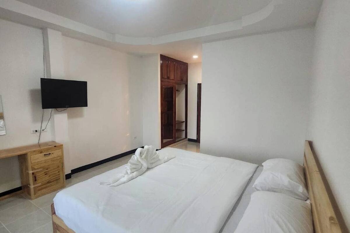 A bedroom with a wooden bed, a TV mounted on the wall, a wooden desk, and a wardrobe.