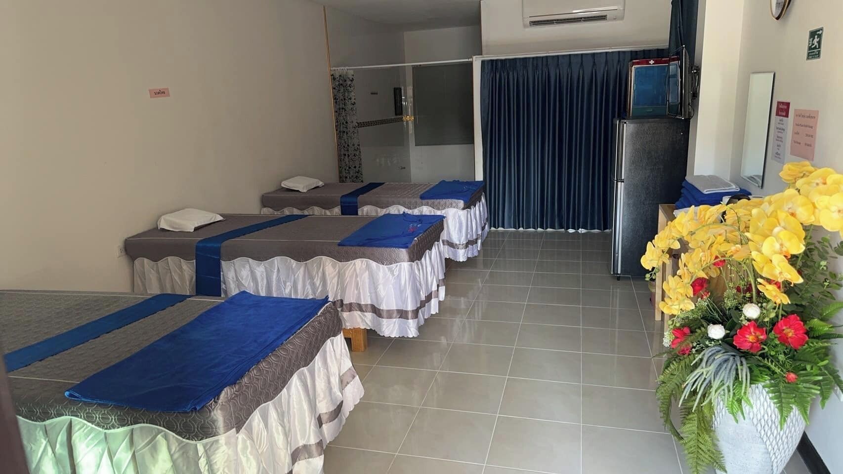 A hotel room with four beds, a small refrigerator, a mirror, and a flower arrangement.
