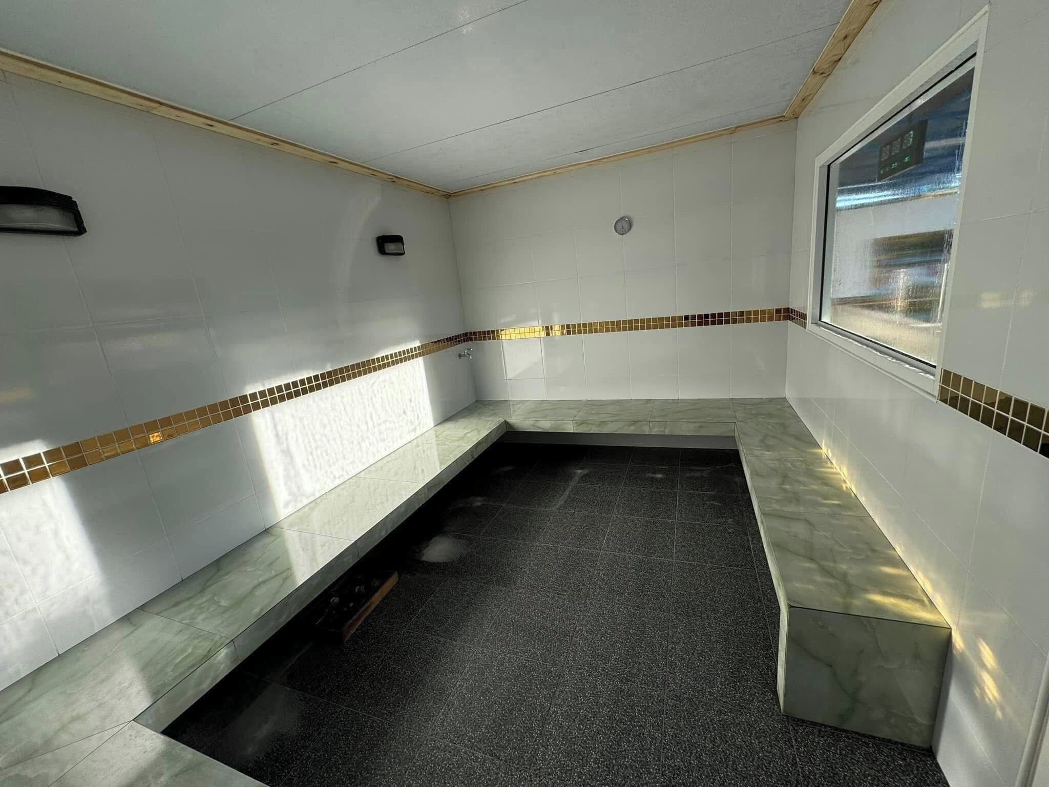 A bathroom with white walls, a black floor, and a bench. There is a window with a view of the outside.