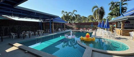 A swimming pool with lounge chairs and umbrellas, surrounded by palm trees and a covered seating area.