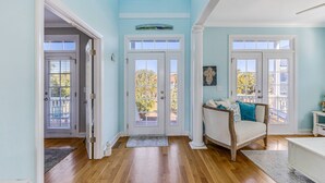 Ein Zimmer mit Holzboden, einem weißen Sofa, einem weißen Konsolentisch und einer Tür zu einem Balkon.