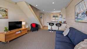 A modern living room with a TV, sofa, and a kitchen area with a bar. - SOHO Vibes - 2 Bedroom Unit (South Hobart)