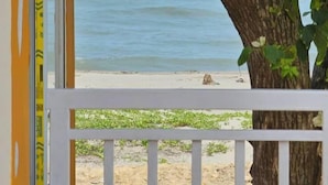 Une vue sur l’océan, encadrée par une fenêtre et un arbre aux fleurs blanches, avec une plage visible au loin.