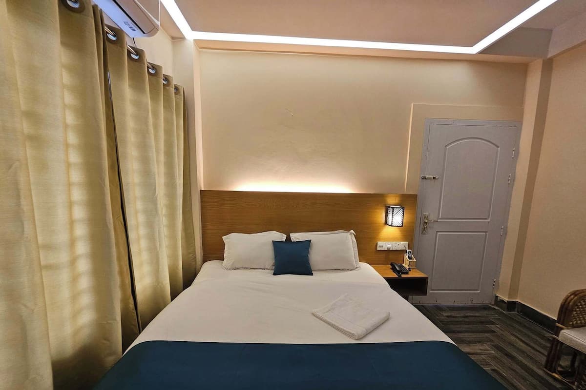 Ein Hotelzimmer mit einem ordentlich bezogenen Bett, einer Nachttischlampe, einer Tür und einem kleinen Tisch mit einem Telefon.