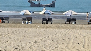 Une plage avec plusieurs chaises longues et des parasols, un grand bateau sur l’eau et une vue dégagée sur l’océan.
