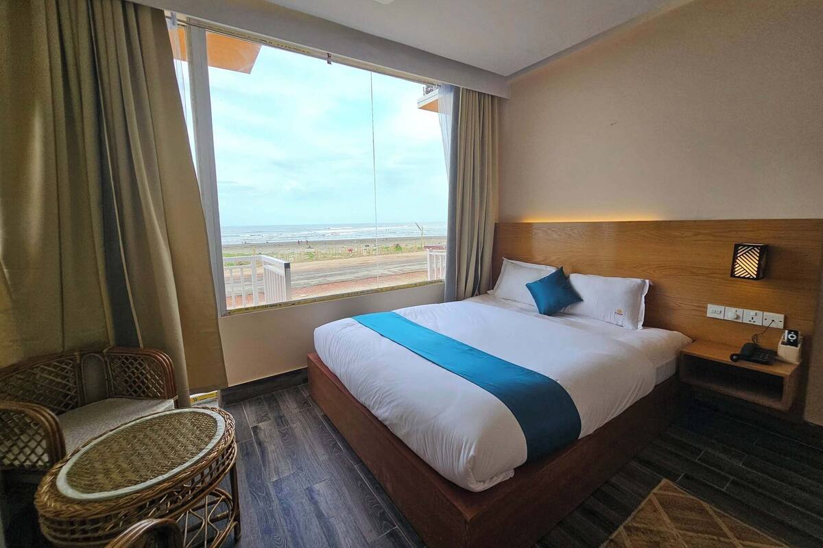 Ein Hotelzimmer mit einem großen Bett, einem Sessel, einem Nachttisch und Blick auf den Strand.