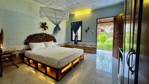 A bedroom with a bed on a wooden platform, a decorative headboard, a mosquito net, and a view of greenery through the window. - Mương Đình Lodge (Can Tho)
