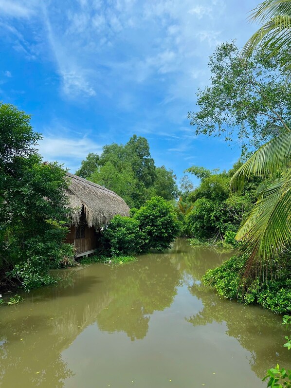 Una capanna con tetto di paglia circondata da rigogliosa vegetazione e un fiume tranquillo.