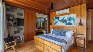 A modern bedroom with a wooden ceiling, a large bed with patterned bedding, a side table, and a wall-mounted air conditioner.
