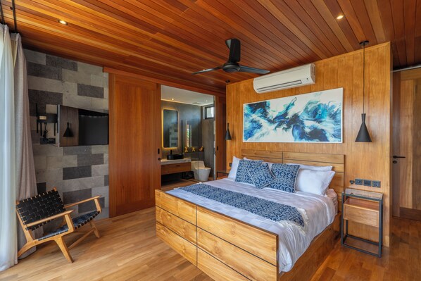 A modern bedroom with a wooden ceiling, a large bed with patterned bedding, a side table, and a wall-mounted air conditioner.