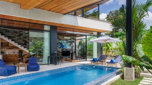 A modern outdoor pool area with a glass-enclosed staircase, seating, and a TV.