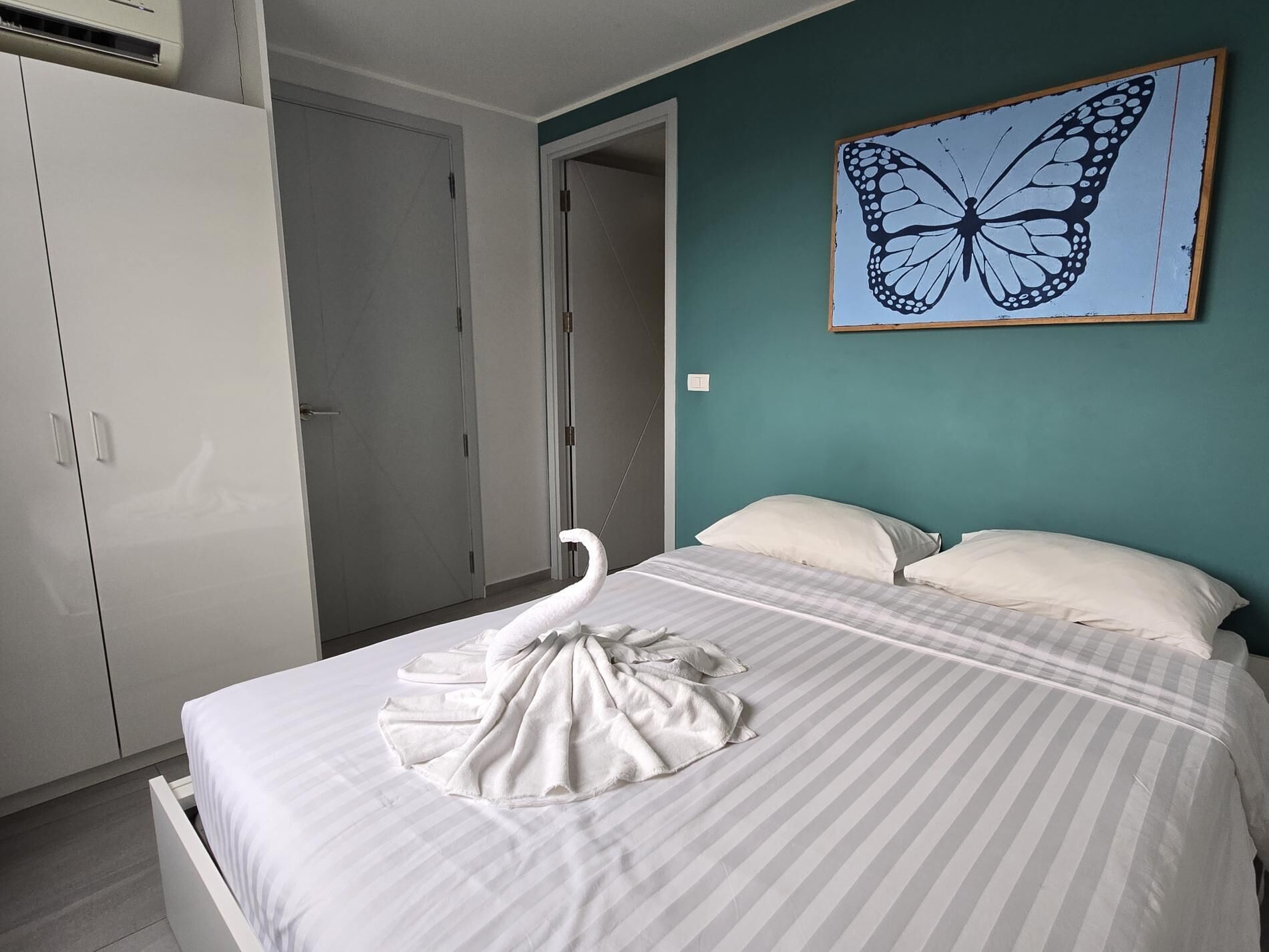 Una camera d'albergo con un letto, un asciugamano a forma di cigno, un quadro con farfalle e un armadio.