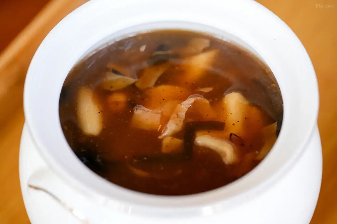 A white bowl containing a clear broth with vegetables.