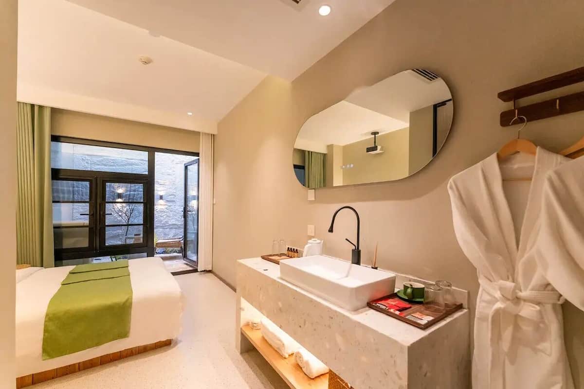Quarto de hotel com cama, banheiro com pia e espelho, e vista para o exterior.