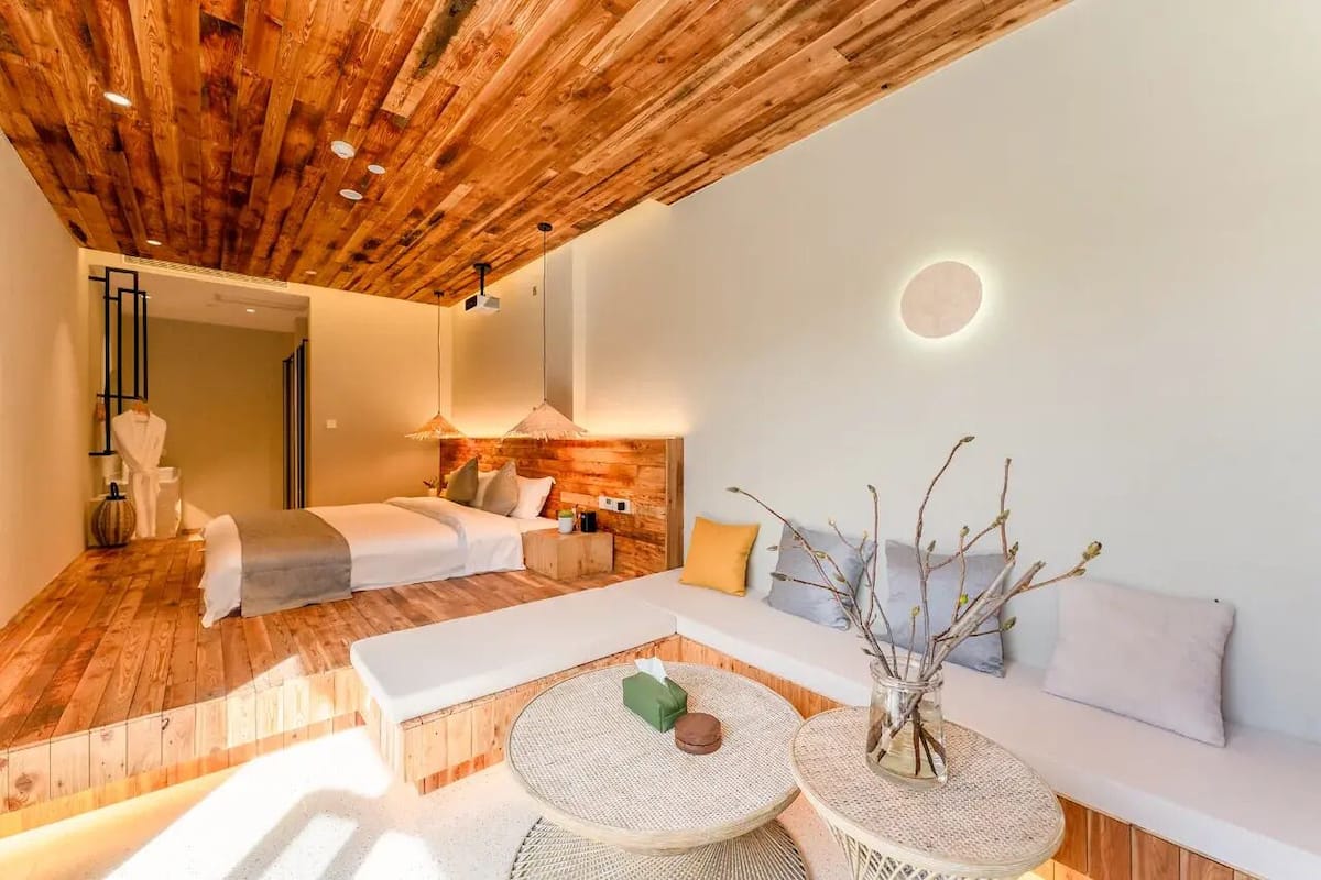 Quarto moderno com teto de madeira, uma cama, um sofá e uma mesa redonda com um vaso.