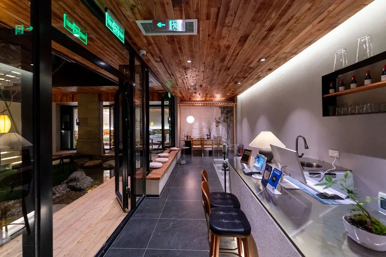 A modern interior with a wooden ceiling, a reception desk, and a seating area with a view of a garden.