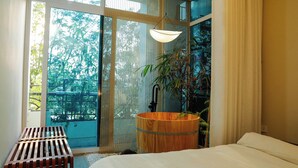 A bedroom with a large bed, a wooden stool, a hanging light fixture, and a view of trees through large windows. - Home. Homestay (Hanoi)