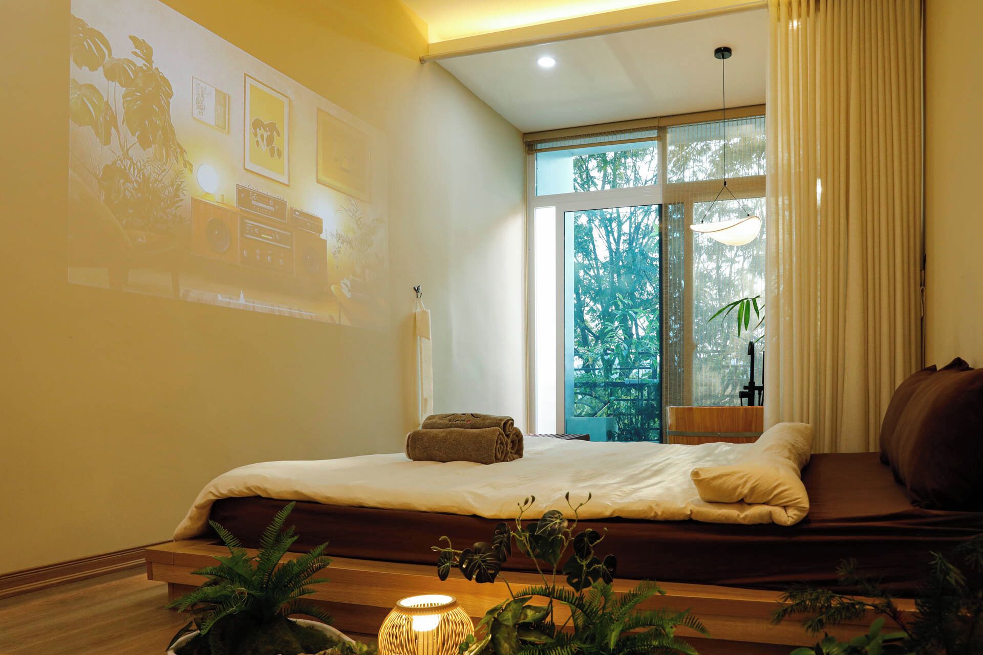 A room with a bed, a large window, and a projector screen on the wall.