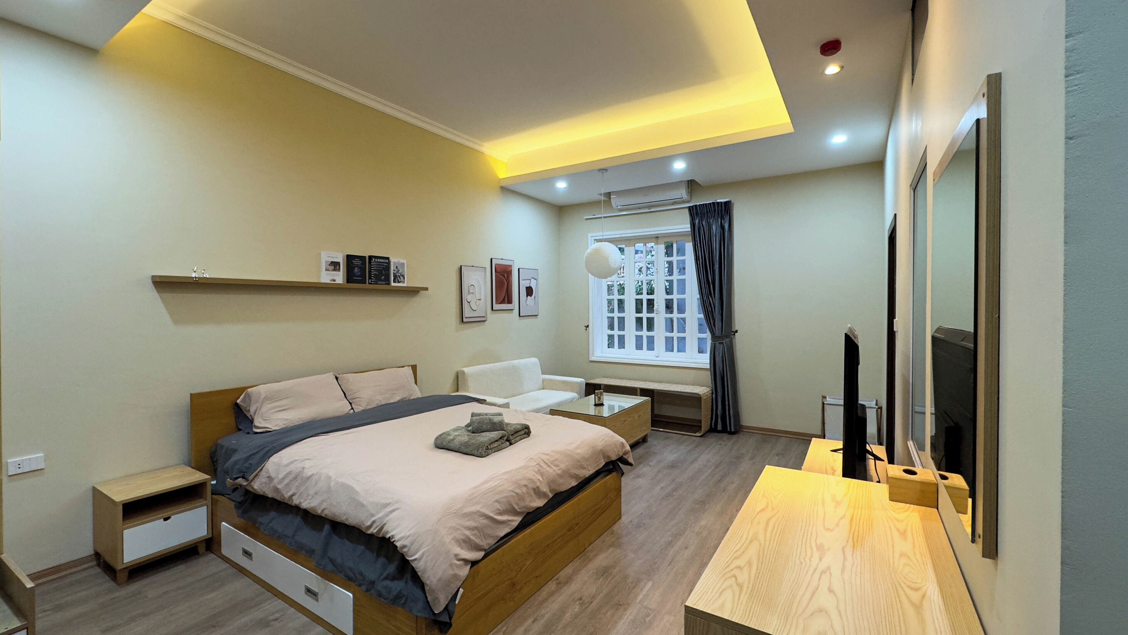 A modern bedroom with a bed, bedside tables, a sofa, a TV, and a window with curtains.