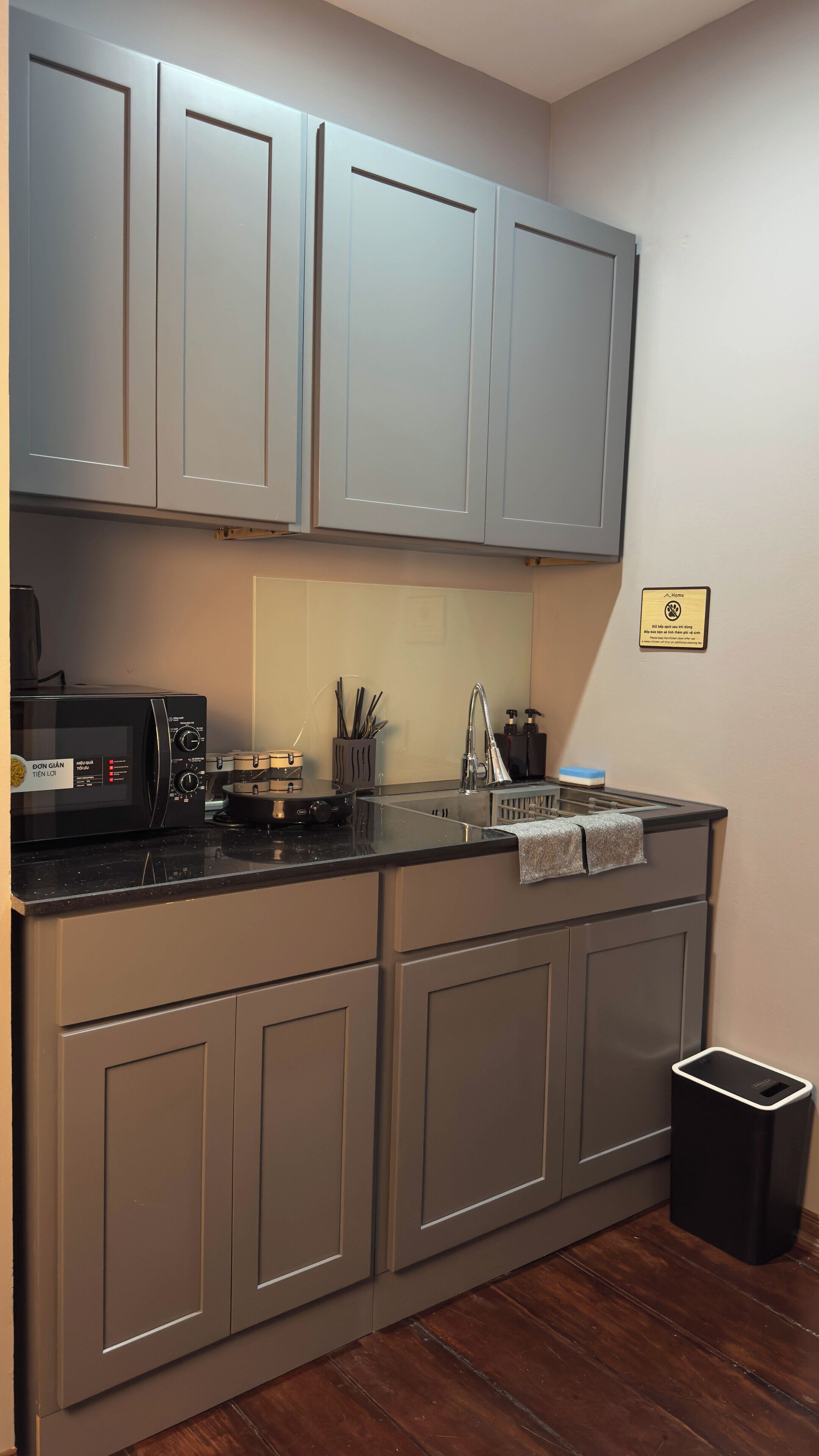 A kitchen with grey cabinets, a black microwave, and a stainless steel sink.
